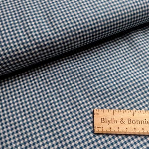 May include: A close-up shot of blue and white gingham fabric. A wooden ruler with the text "Blyth & Bonnie" is in the foreground. The fabric is folded, revealing the texture and pattern of the material.