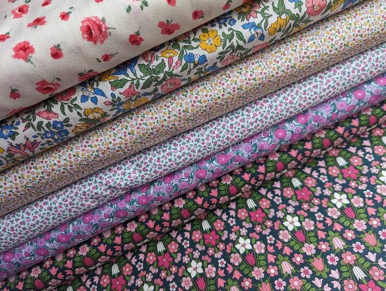 Pode incluir: Um conjunto de seis amostras de tecido com diferentes padr&otilde;es florais. A amostra superior &eacute; branca com rosas cor-de-rosa, a segunda &eacute; branca com flores azuis e amarelas, a terceira &eacute; branca com flores cor-de-rosa e amarelas, a quarta &eacute; branca com flores cor-de-rosa e roxas, a quinta &eacute; branca com flores cor-de-rosa e verdes, e a amostra inferior &eacute; azul escuro com flores cor-de-rosa e brancas.