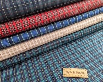 May include: A stack of six folded fabric bolts featuring various plaid patterns in red, blue, green, and beige with thin yellow and white lines. A wooden ruler with the text Blyth & Bonnie is placed on the fabric, showing a length of 8 inches.