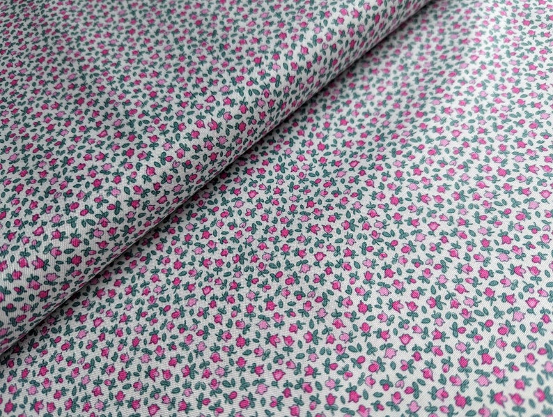 Pode incluir: Tecido branco com uma pequena estampa floral rosa e verde. O tecido est&aacute; dobrado ao meio, mostrando o padr&atilde;o em ambos os lados.
