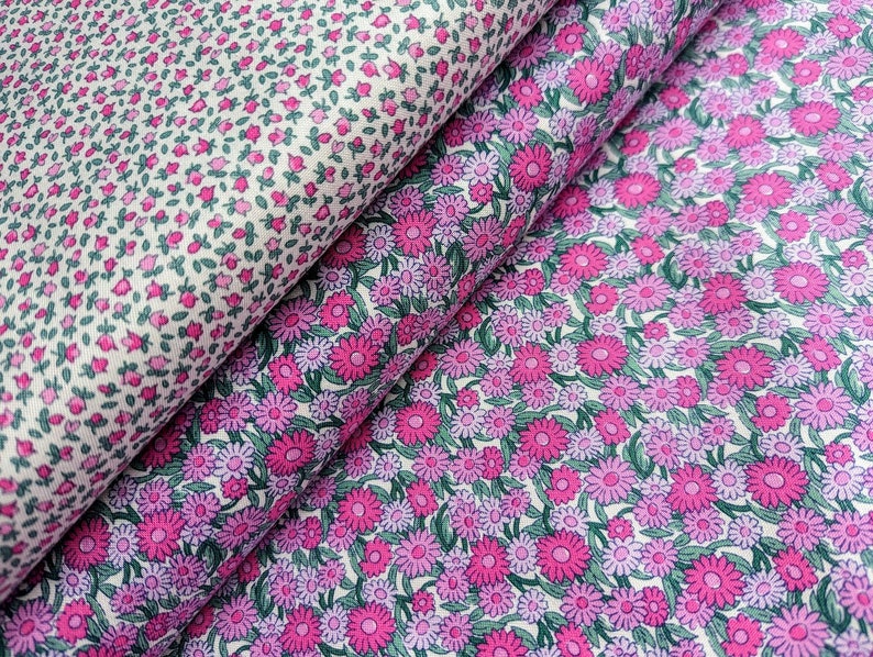 Pode incluir: Duas pe&ccedil;as de tecido com padr&atilde;o floral. Um tecido tem um fundo branco com pequenas flores cor-de-rosa e folhas verdes. O outro tecido tem um fundo branco com flores cor-de-rosa e roxas maiores e folhas verdes.