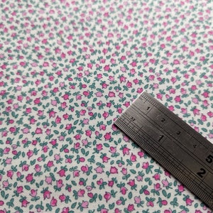 Pode incluir: Tecido branco com um padr&atilde;o repetitivo de pequenas flores cor-de-rosa com folhas verdes. Uma r&eacute;gua de metal &eacute; colocada sobre o tecido, mostrando a escala em cent&iacute;metros.
