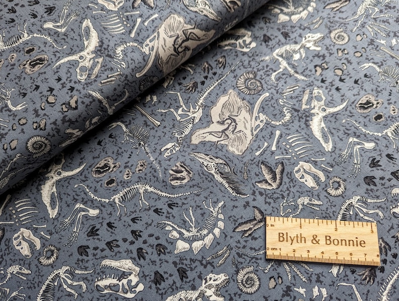May include: Blue fabric with a white dinosaur skeleton print. The fabric features a variety of dinosaur bones, fossils, and footprints. The fabric is perfect for crafting projects, quilting, and home decor.
