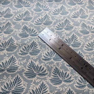 Pode incluir: Um close-up de um tecido azul e branco com um padr&atilde;o repetido de folhas de samambaia. Uma r&eacute;gua de metal &eacute; colocada em cima do tecido, mostrando medidas em polegadas.