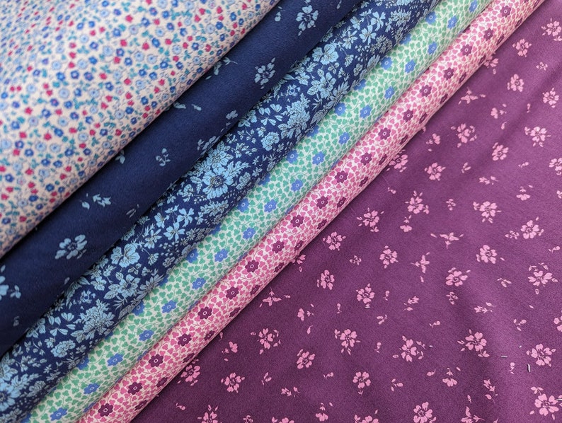 Pode incluir: Cinco amostras de tecido com diferentes padr&otilde;es florais. As amostras est&atilde;o empilhadas, com a parte superior sendo um rosa claro com pequenas flores azuis, seguido de um azul escuro com pequenas flores brancas, depois um verde claro com pequenas flores azuis, depois um rosa claro com pequenas flores brancas, e finalmente um roxo escuro com pequenas flores rosas.