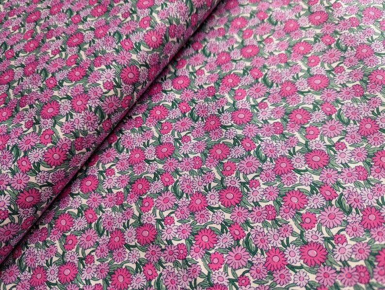 Pode incluir: Tecido floral rosa e roxo com fundo branco. O tecido &eacute; coberto por pequenas flores com folhas verdes.