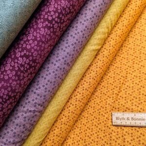 Puede incluir: Rollos de tela en varios colores, incluyendo verde azulado, morado oscuro, lavanda, amarillo y naranja. Las telas presentan patrones florales y geom&eacute;tricos. Se ve una regla de madera con el texto "Blyth & Bonnie".