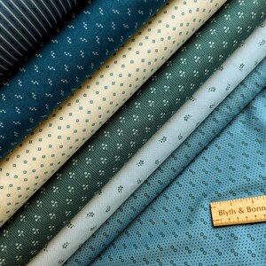 Puede incluir: Una variedad de rollos de tela en tonos de azul, verde y crema. Las telas presentan peque&ntilde;os patrones repetidos de puntos y formas florales. Una regla de madera con el texto "Blyth & Bonnie" descansa sobre la tela.