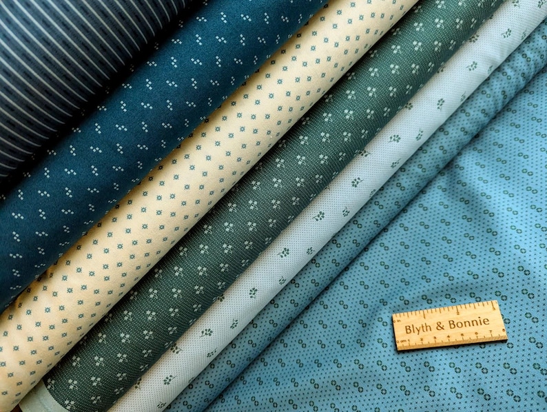Puede incluir: Una variedad de rollos de tela en tonos de azul, verde y crema. Las telas presentan peque&ntilde;os patrones repetidos de puntos y formas florales. Una regla de madera con el texto "Blyth & Bonnie" descansa sobre la tela.