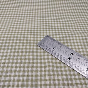 Puede incluir: Primer plano de una tela de vichy verde y blanca con una regla que mide 7,6 cm. La tela tiene un pequeño patrón de cuadros.