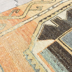 May include: A vintage rug with a geometric pattern in shades of orange, brown, blue, and white. The rug has a distressed look and is made of wool.