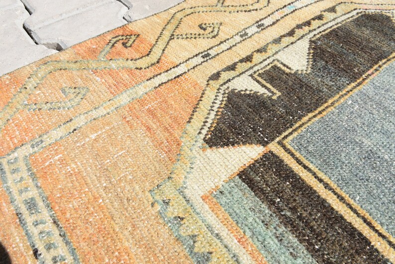 May include: A vintage rug with a geometric pattern in shades of orange, brown, blue, and white. The rug has a distressed look and is made of wool.