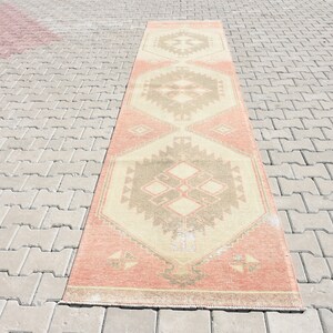Puede incluir: Una alfombra larga y rectangular con un patr&oacute;n geom&eacute;trico en tonos melocot&oacute;n, beige y marr&oacute;n. La alfombra tiene un aspecto desgastado y vintage.