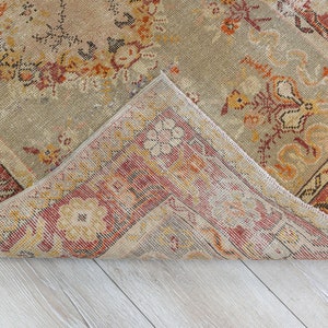 Puede incluir: Una alfombra vintage con un patr&oacute;n floral descolorido en tonos rojos, naranjas y beige. La alfombra tiene un aspecto desgastado y deteriorado y est&aacute; doblada por la mitad, revelando la parte inferior.