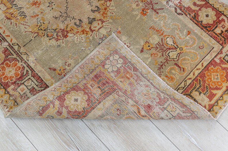 Puede incluir: Una alfombra vintage con un patr&oacute;n floral descolorido en tonos rojos, naranjas y beige. La alfombra tiene un aspecto desgastado y deteriorado y est&aacute; doblada por la mitad, revelando la parte inferior.