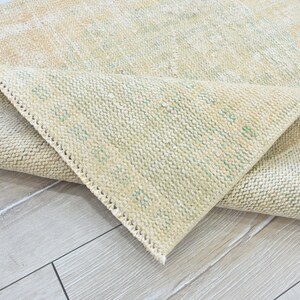 May include: A close-up of a beige rug with a subtle green pattern. The rug is folded in half, revealing the underside of the fabric.