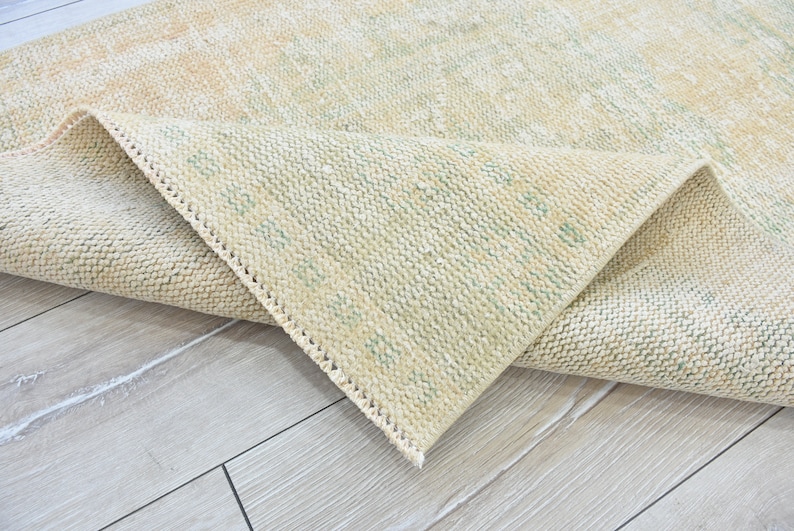 May include: A close-up of a beige rug with a subtle green pattern. The rug is folded in half, revealing the underside of the fabric.