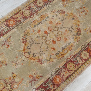 Puede incluir: Una alfombra vintage con fondo beige y intrincados patrones florales en tonos rojos, naranjas y marrones. La alfombra tiene un aspecto descolorido y desgastado, lo que le da un toque &uacute;nico y antiguo.