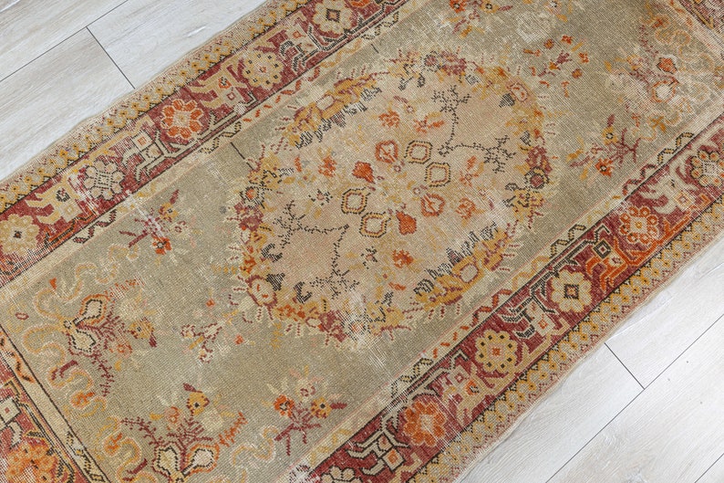 Puede incluir: Una alfombra vintage con fondo beige y intrincados patrones florales en tonos rojos, naranjas y marrones. La alfombra tiene un aspecto descolorido y desgastado, lo que le da un toque &uacute;nico y antiguo.