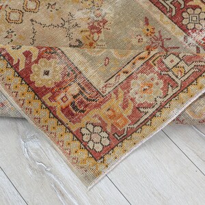 Puede incluir: Una alfombra vintage con fondo beige y un patr&oacute;n geom&eacute;trico rojo, naranja y amarillo. La alfombra est&aacute; doblada por la mitad, mostrando la parte inferior.