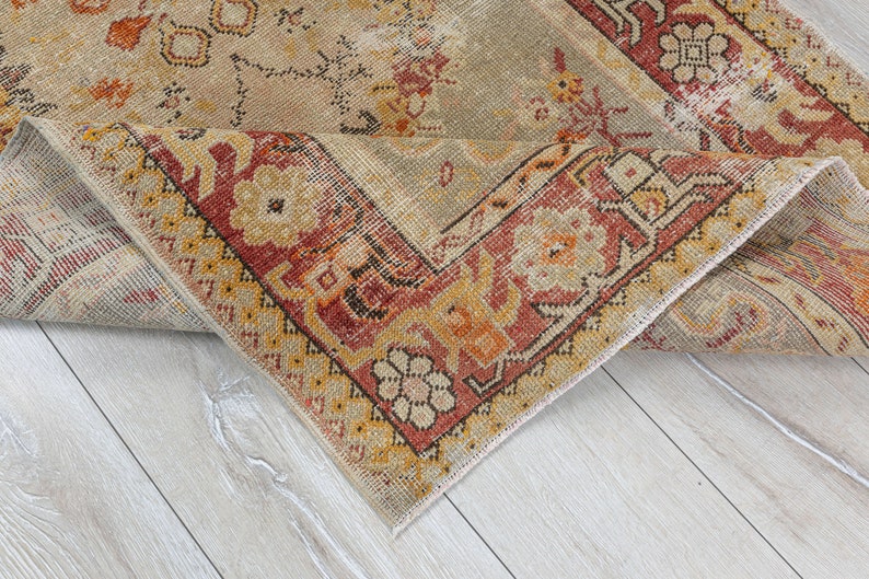 Puede incluir: Una alfombra vintage con fondo beige y un patr&oacute;n geom&eacute;trico rojo, naranja y amarillo. La alfombra est&aacute; doblada por la mitad, mostrando la parte inferior.