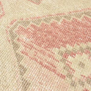 Puede incluir: Primer plano de una alfombra tejida con un patr&oacute;n geom&eacute;trico rosa y beige. La alfombra tiene una superficie suave y texturizada.