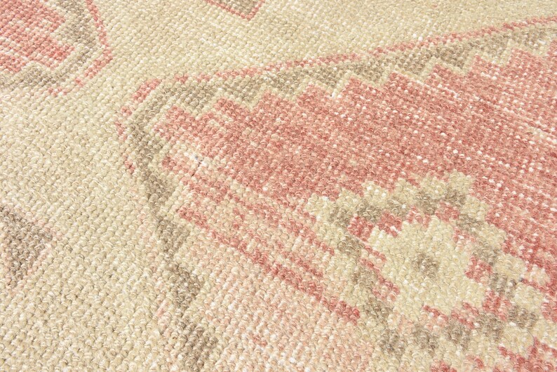 Puede incluir: Primer plano de una alfombra tejida con un patr&oacute;n geom&eacute;trico rosa y beige. La alfombra tiene una superficie suave y texturizada.
