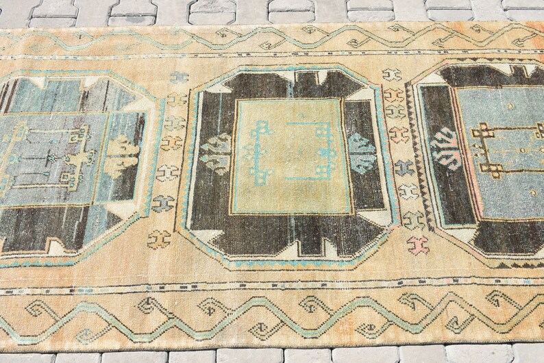 May include: A vintage rug with a beige background and intricate patterns in shades of brown, blue, and green. The rug features a central design with a square shape and a border of geometric motifs.