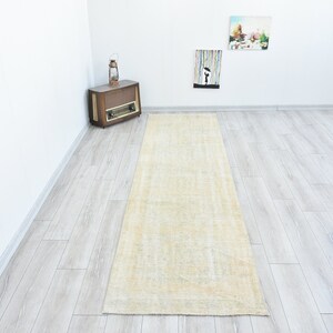 May include: A light beige runner rug with a subtle pattern. The rug is laid out on a light gray wood floor.