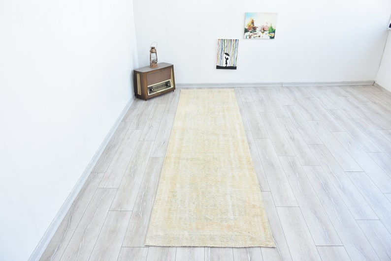 May include: A light beige runner rug with a subtle pattern. The rug is laid out on a light gray wood floor.