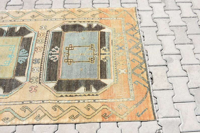 May include: A vintage rug with a geometric pattern in shades of beige, brown, blue, and pink. The rug has a fringe border and is laid out on a gray concrete surface.