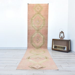 Puede incluir: Una alfombra de pasillo rosa y beige con un patrón geométrico. La alfombra tiene un diseño tradicional con detalles intrincados.
