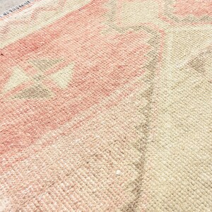 Puede incluir: Primer plano de una alfombra tejida con un patr&oacute;n rosa y beige. La alfombra tiene flecos en el borde.