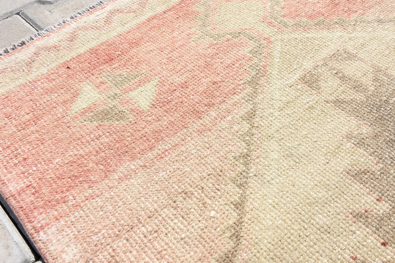 Puede incluir: Primer plano de una alfombra tejida con un patr&oacute;n rosa y beige. La alfombra tiene flecos en el borde.
