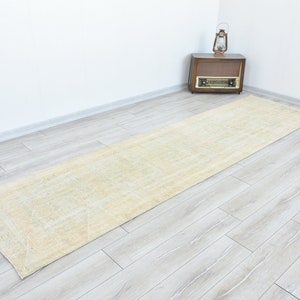 May include: A light beige runner rug with a subtle pattern. The rug is laid out on a light wood floor.