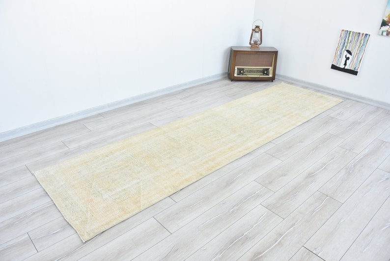 May include: A light beige runner rug with a subtle pattern. The rug is laid out on a light wood floor.