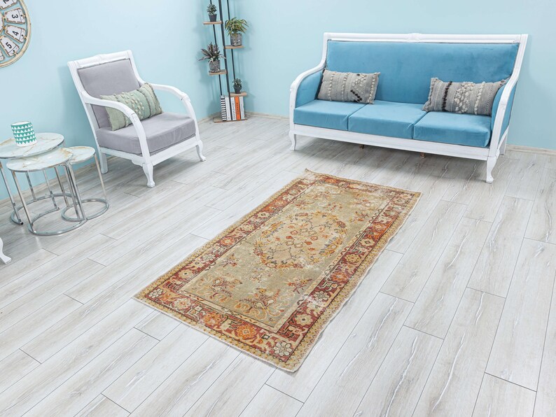 Puede incluir: Una alfombra vintage con fondo beige y un patr&oacute;n floral en tonos naranja, rojo y marr&oacute;n. La alfombra est&aacute; colocada sobre un suelo de madera clara en una habitaci&oacute;n con muebles blancos.