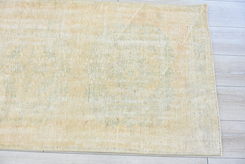 May include: A light beige rug with a faded, light green pattern. The rug has a subtle distressed look and a woven texture.