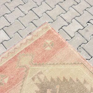 Puede incluir: Una alfombra vintage con un patr&oacute;n geom&eacute;trico en tonos rosa, beige y gris. La alfombra est&aacute; colocada sobre una superficie de hormig&oacute;n gris.