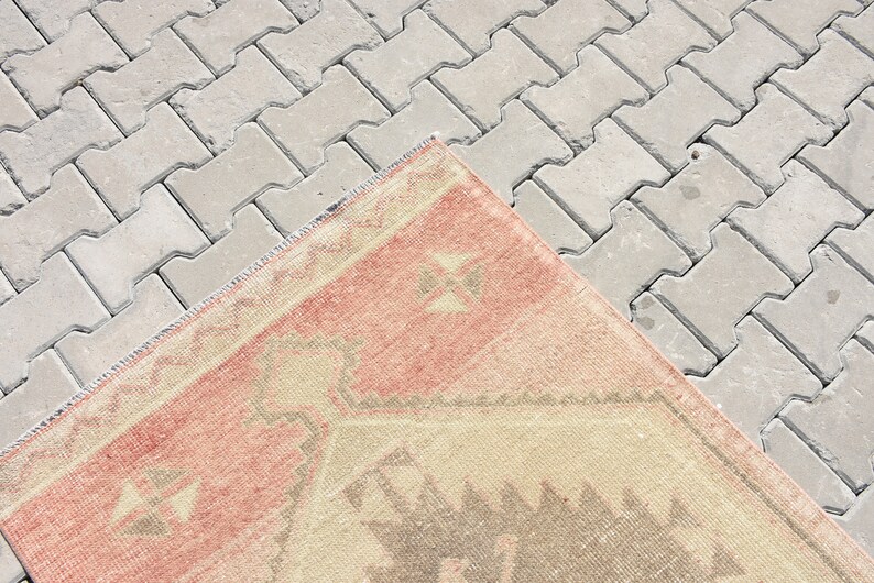 Puede incluir: Una alfombra vintage con un patr&oacute;n geom&eacute;trico en tonos rosa, beige y gris. La alfombra est&aacute; colocada sobre una superficie de hormig&oacute;n gris.