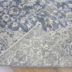 May include: Close-up of a corner of a blue and cream patterned rug with a floral design. The rug has a distressed, vintage look.
