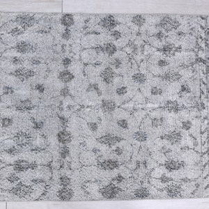 May include: A gray and white patterned rug with a floral design. The rug has a distressed look and is made of a soft, woven material.