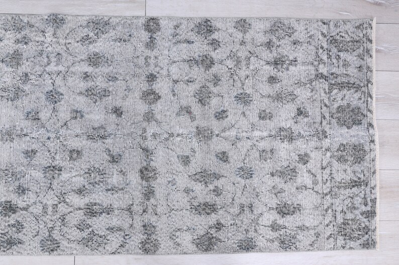 May include: A gray and white patterned rug with a floral design. The rug has a distressed look and is made of a soft, woven material.