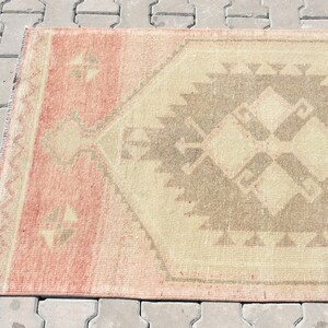 Puede incluir: Una alfombra vintage con un patr&oacute;n geom&eacute;trico en tonos rosa, beige y marr&oacute;n. La alfombra tiene un aspecto desgastado y es perfecta para a&ntilde;adir un toque de estilo bohemio a cualquier habitaci&oacute;n.