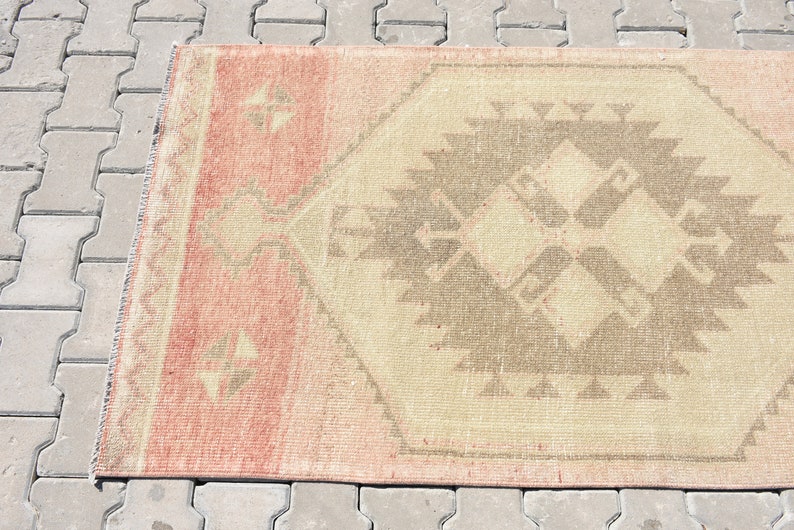 Puede incluir: Una alfombra vintage con un patr&oacute;n geom&eacute;trico en tonos rosa, beige y marr&oacute;n. La alfombra tiene un aspecto desgastado y es perfecta para a&ntilde;adir un toque de estilo bohemio a cualquier habitaci&oacute;n.