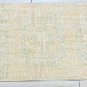 May include: A light yellow rug with a subtle green pattern. The rug has a distressed look and is made of a soft, woven material.