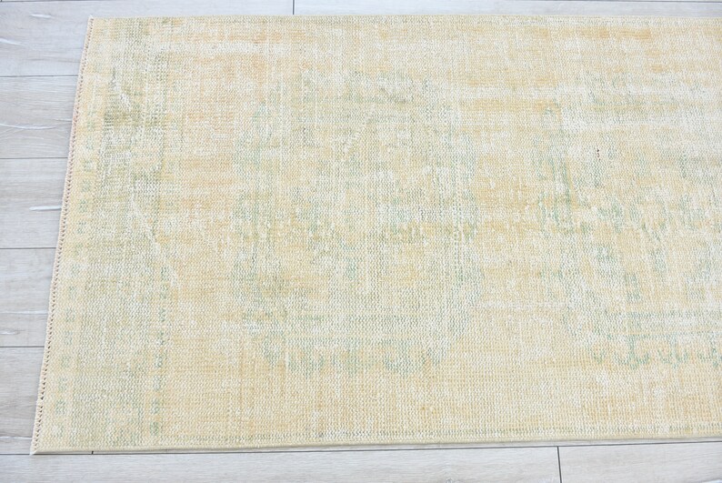 May include: A light yellow rug with a subtle green pattern. The rug has a distressed look and is made of a soft, woven material.