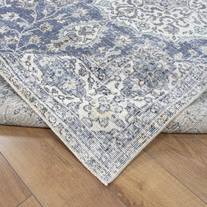 May include: Close-up of a blue and cream patterned rug with a detailed floral design. The rug is folded over to show the underside of the fabric.