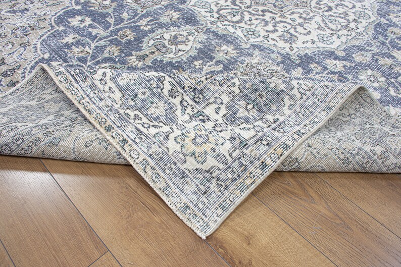 May include: Close-up of a blue and cream patterned rug with a detailed floral design. The rug is folded over to show the underside of the fabric.