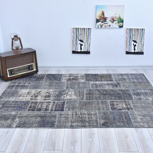 May include: A gray and blue patchwork rug with a distressed look. The rug is made of different pieces of fabric sewn together. It is laid out on a light wood floor.